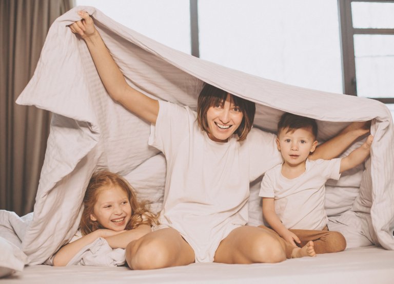 Mère avec son fils et sa fille assis sur un lit sous une couverture